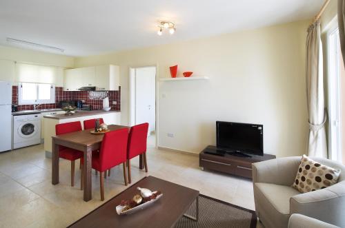 a living room with a table and red chairs and a kitchen at Club St. George in Paphos City