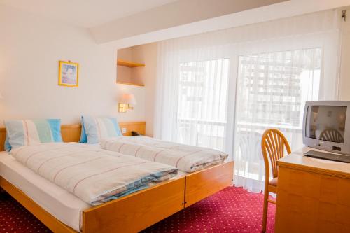 a bedroom with a bed and a tv and a window at Hotel Heilquelle-Leukerbad-Therme in Leukerbad