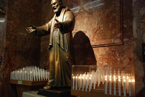 a statue of a man standing next to a bunch of candles at Albergo Villa Marchese in San Giovanni Rotondo