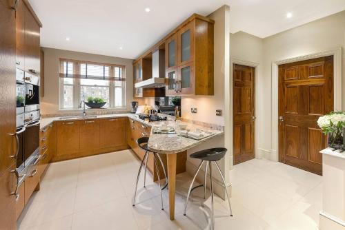 a kitchen with wooden cabinets and a island with bar stools at Grand Ambassadorial Duplex Apartment Hyde Park in London
