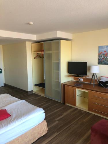 ein Hotelzimmer mit einem Bett und einem Schreibtisch mit einem TV in der Unterkunft Nordseehotel Benser Hof am Hafen in Bensersiel