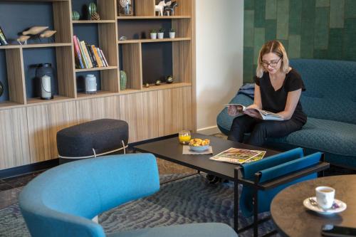 a woman sitting on a couch reading a book at Mercure Cavaillon in Cavaillon