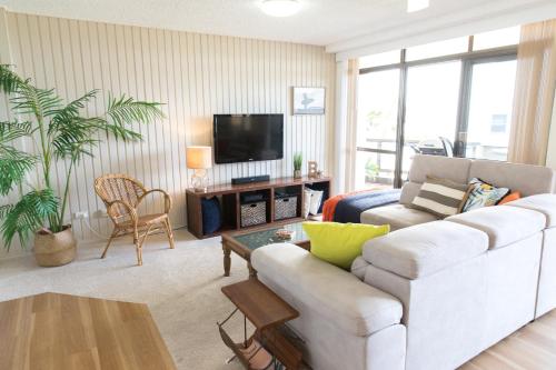 a living room with a white couch and a tv at Beauty at the Beach - modern beachfront apartment in Port Macquarie