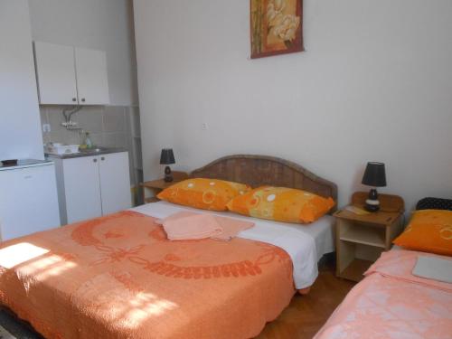 a bedroom with two beds with orange pillows and a kitchen at Apartments & Hostel Zdrava Hrana in Mostar