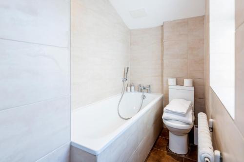 a white bathroom with a toilet and a bath tub at Elegant 3Bed Apartment in Kensington Olympia in London