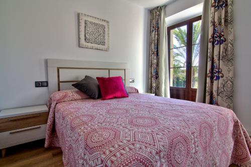 a bedroom with a bed with a pink blanket and a window at Apartamentos Arenal in Jerez de la Frontera