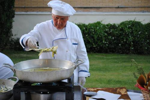 a chef preparing food in a pan on a grill at Hotel Holiday Sul Lago in Bolsena