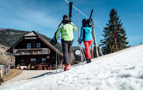 two people walking up a snow covered slope in front of a cabin at Der Kirchheimerhof - Superior in Bad Kleinkirchheim