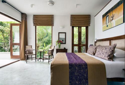 a bedroom with a bed and chairs and windows at Rosyth Estate House in Pinnawala