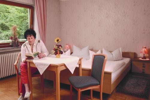 a woman sitting at a table reading a book at Pension Burk in Bad Endbach