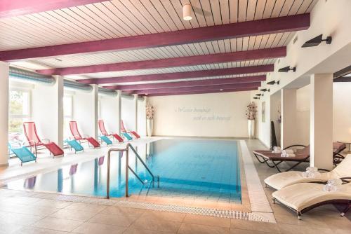 a swimming pool in a hotel with red chairs at Hotel Steirerrast in Kaindorf