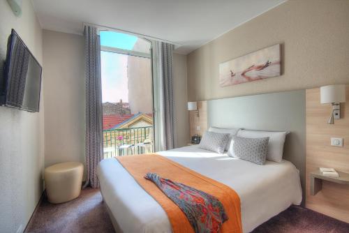 ニースにあるホテル デュ ミディのベッドと大きな窓が備わるホテルルームです。