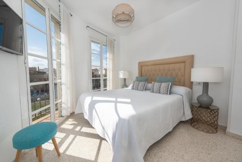 a white bedroom with a bed and a blue chair at Myramar Premium Center in Málaga