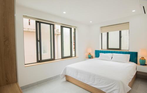 a white bedroom with a bed and windows at Kim Phu Villa Hoi An in Hoi An