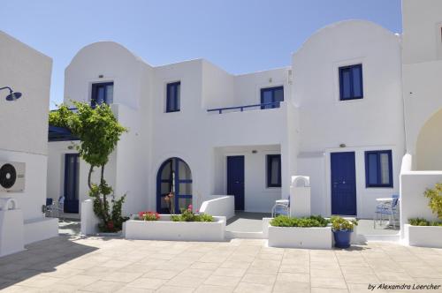 a courtyard with white buildings with blue doors and plants at Olympic Villas in Oia