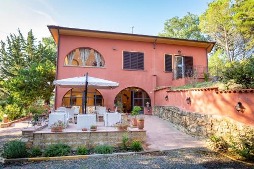 une maison orange avec des chaises blanches et un parasol dans l'établissement Podere San Filippo B&B-Apartment-Pet Friendly-Rent Bike and Bike Friendly, à Bibbona