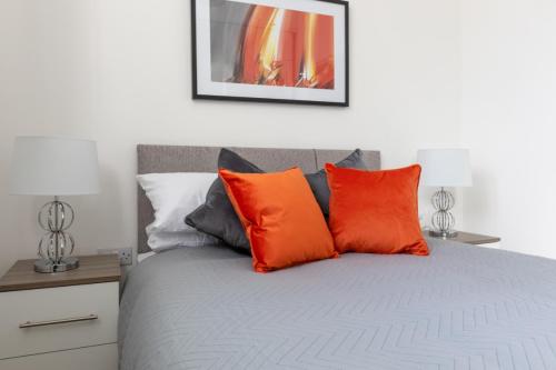 Una cama con almohadas de color naranja y gris. en Charlie Mews en Farnborough