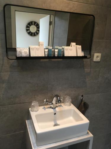 een wastafel in de badkamer met een spiegel en een klok bij Studio 't Ponton in Nieuwpoort