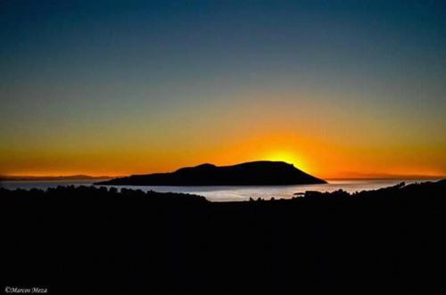a sunset over the ocean with a mountain in the distance at Amantani Lodge in Amantani