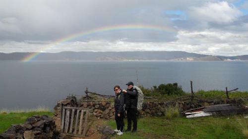 two people standing on a hill with a rainbow in the background at Amantani Lodge in Amantani