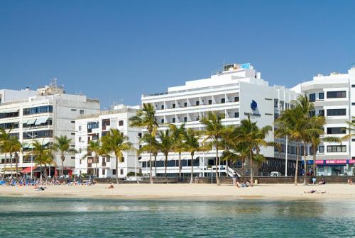 
a beach with palm trees and a large building at Hotel Lancelot in Arrecife
