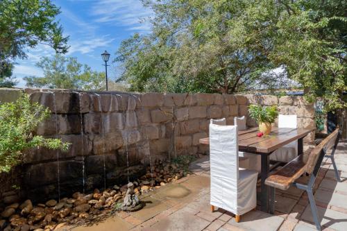 a stone retaining wall with a wooden table and chairs at De Zeekoe Guest Farm in Oudtshoorn