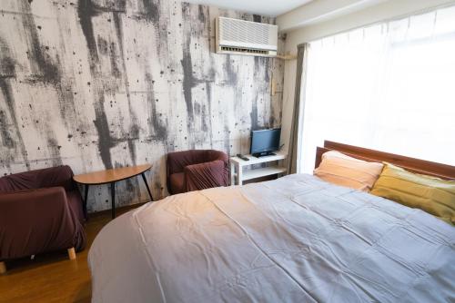a bedroom with a bed and two chairs and a television at SONIC APARTMENT HOTEL in Dazaifu