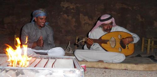 two men sitting next to a fire with a guitar at Real Bedouin Experience Tours & Camp in Wadi Rum