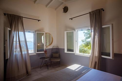a bedroom with a bed and two windows and a chair at Avali luxury houses in Gaios