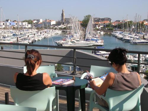 two women sitting at a table on a balcony overlooking a marina at TERNELIA Le Vent Du Large in Saint-Gilles-Croix-de-Vie