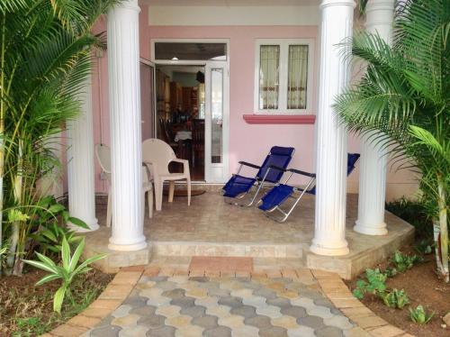 a pink house with white columns and blue chairs at Fayruz Villa is a 3 bedroom, 3 bathroom detached house with AC and swimming pool 5 minutes walk from Flic en Flac public beach in Flic-en-Flac