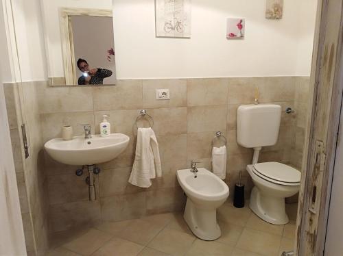 une personne prenant une photo d'une salle de bains avec toilettes et lavabo dans l'établissement B&B Le Peonie, à Badesi