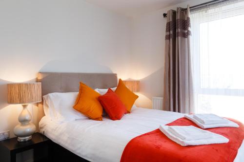 uma cama com almofadas cor-de-laranja e brancas e uma janela em Contemporary Trumpington Apartment with Self Check-in ,FREE On-site Parking, Terrace, SUPER Fast WIFI & 5 mins drive to Papworth & Addenbrookes hospitals em Cambridge