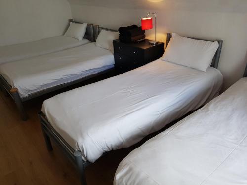 three beds in a room with white sheets and a lamp at Boscombe Reef Hotel in Bournemouth