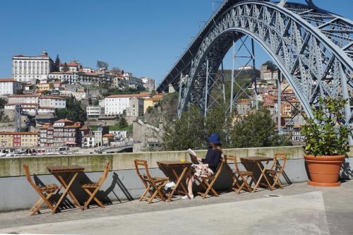 a person sitting on a bench near a bridge at Porto View by Patio 25 in Vila Nova de Gaia