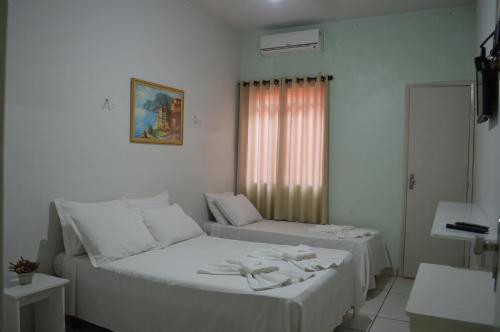 1 dormitorio con 2 camas con sábanas blancas y ventana en Touring Hotel, en Maringá