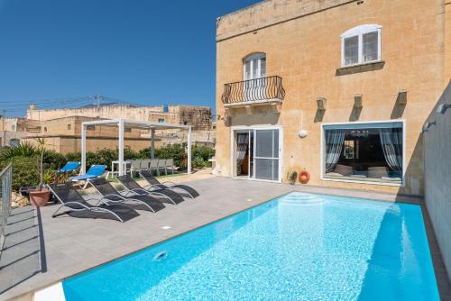 a swimming pool with chairs next to a building at Twilight Holiday Home in Għasri