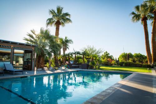 a swimming pool with palm trees and a house at The Spring Resort & Spa in Desert Hot Springs
