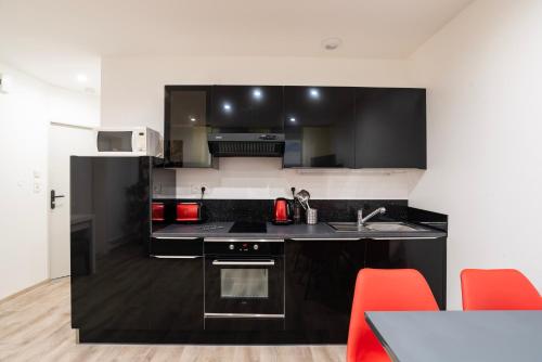 una cocina con armarios blancos y negros y sillas rojas en CityCosy Strasbourg - T2 Hirtz Orangerie, en Estrasburgo