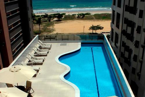 a swimming pool with chairs and umbrellas next to a beach at Flat Executive Beira Mar in Recife