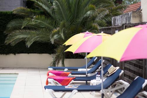 un grupo de sillas con sombrillas junto a una piscina en Hôtel Le Dauphin, en Arcachon