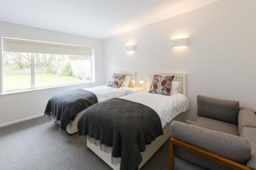 two beds in a room with a window and a chair at Invershin -Aldeburgh Coastal Cottages in Thorpeness