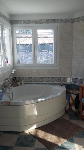 La salle de bains est pourvue d'une baignoire blanche et de 2 fenêtres. dans l'établissement Agréable Maison sur le Bassin d'Arcachon, à Andernos-les-Bains