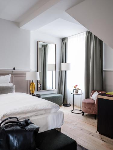 a bedroom with a bed and a chair and a mirror at AMERON Neuschwanstein Alpsee Resort & Spa in Schwangau