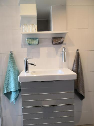 a bathroom with a white sink and white tiles at Studio Callanya in Callantsoog