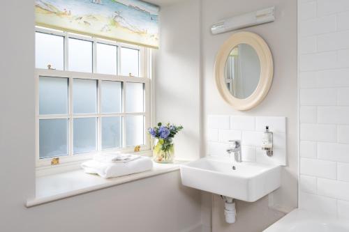 a white bathroom with a sink and a window at The Farmhouse at Bodnant Welsh Food in Conwy