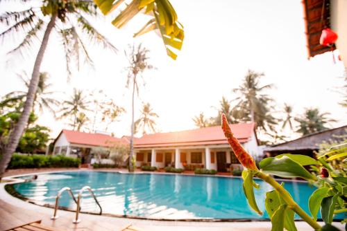 a pool in front of a building with palm trees at Hula Hula Seafront Phu Quoc in Phu Quoc