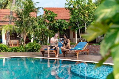 a man and woman sitting next to a swimming pool at Hula Hula Seafront Phu Quoc in Phu Quoc