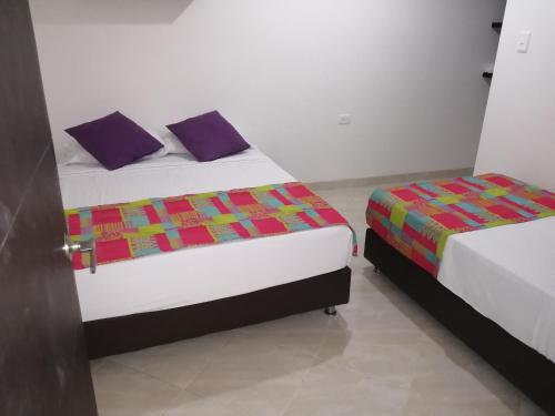 two beds in a small room with purple pillows at Hotel Oasis de la Tatacoa in Villavieja