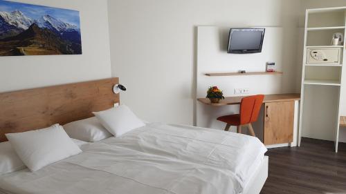 a bedroom with a white bed and a desk and a tv at Hotel Bernerhof in Interlaken